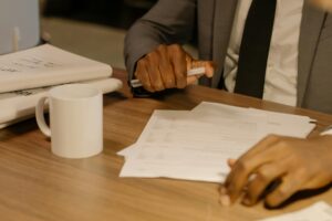 Free Close-up of a businessman holding and reviewing documents on a wooden desk. Stock Photo